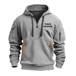 May include: Gray hooded sweatshirt with a quarter-zip closure and orange zipper accents. Features a kangaroo pocket, a small pocket on the left sleeve, and the text "YOUR DESIGN" printed on the chest. The sweatshirt has a drawstring hood.