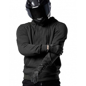 Pode incluir: Um capacete de motocicleta preto com viseira escura e um moletom preto com capuz. A pessoa está usando luvas de couro pretas. A imagem é contra um fundo branco.