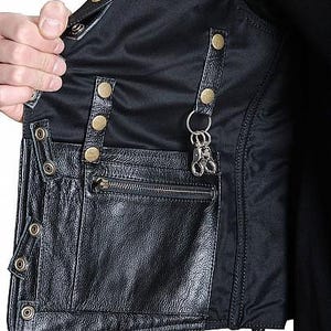 May include: Black leather vest with multiple pockets, metal snap closures, and a zipper pocket. The vest has a black nylon lining and a metal key ring attached to the inside. The vest is shown open, revealing the interior.