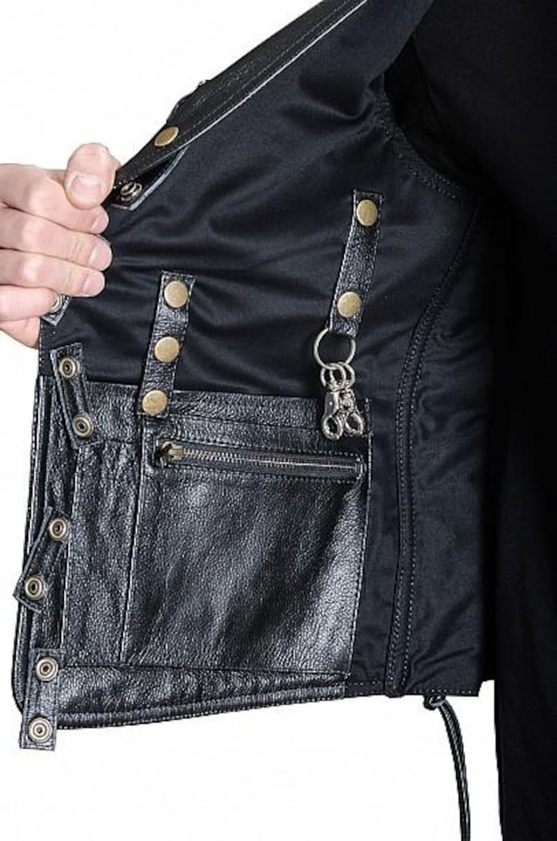 May include: Black leather vest with multiple pockets, metal snap closures, and a zipper pocket. The vest has a black nylon lining and a metal key ring attached to the inside. The vest is shown open, revealing the interior.