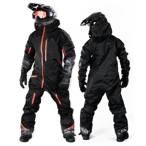 Op de afbeelding: Zwart sneeuwscooterpak met oranje ritsen en accenten. Het pak heeft een capuchon, handschoenen en een helm met oranje getinte glazen. Ontworpen voor koud weer en buitenactiviteiten.