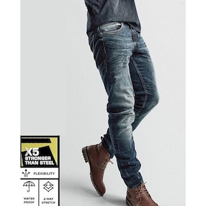 Op de afbeelding: Verbleekte blauwe jeans met een lichte wassing en een slanke pasvorm. De jeans wordt gecombineerd met bruine leren laarzen. De afbeelding bevat ook de tekst "X5 STRONGER THAN STEEL", "FLEXIBILITY", "WATER PROOF" en "2-WAY STRETCH".