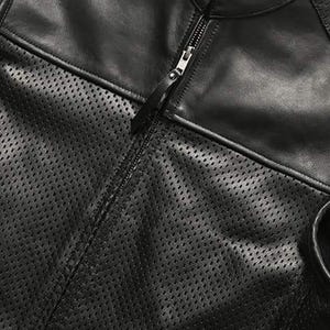 May include: Close-up of a black leather jacket with a perforated design on the front panel. The jacket features a full zipper closure and a smooth leather section on the upper chest and shoulders.