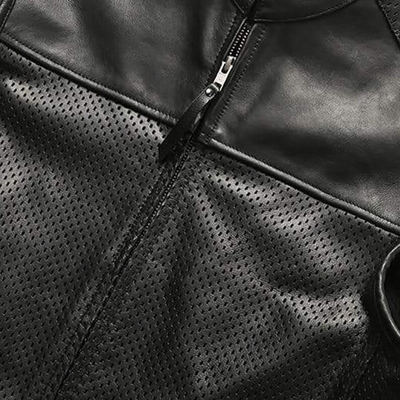 May include: Close-up of a black leather jacket with a perforated design on the front panel. The jacket features a full zipper closure and a smooth leather section on the upper chest and shoulders.