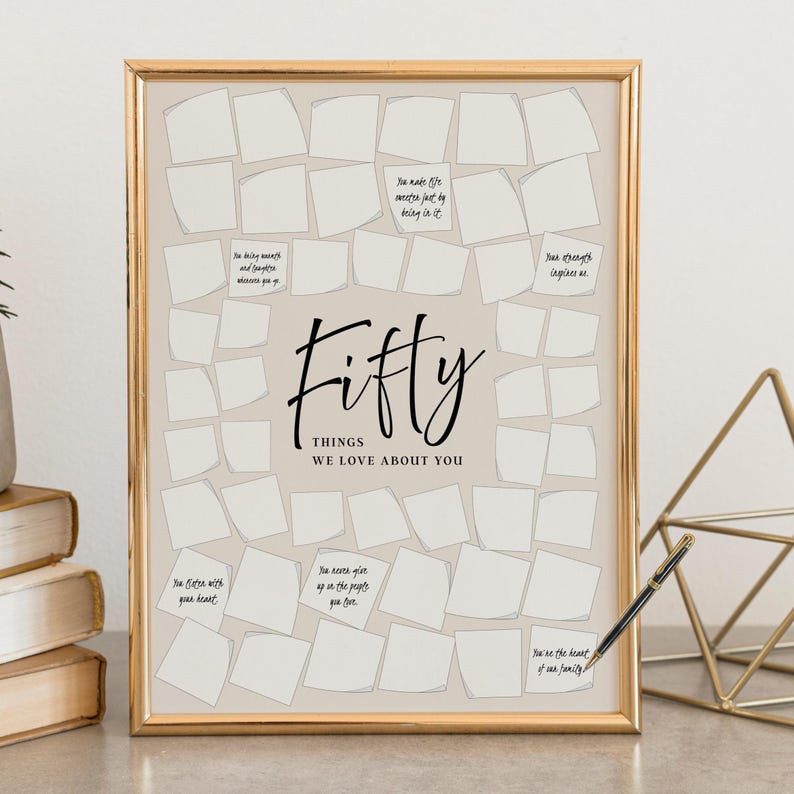 May include: A framed print with a gold frame and a beige background. The print features the word "Fifty" in a stylish font, with the text "THINGS WE LOVE ABOUT YOU" below it. Small white notes are arranged around the text, with handwritten phrases.