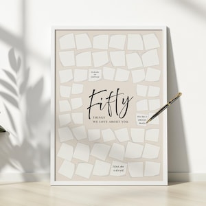 May include: A framed print with the words "Fifty Things We Love About You" in elegant script. The print features a beige background with numerous blank, torn paper-like squares. A gold and black pen rests on the frame.