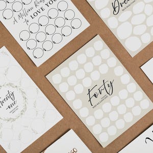 May include: A collection of white cards with various designs and text, including floral illustrations, the word "Forty," and anniversary details. The cards are arranged on a brown surface, creating a visually appealing display.