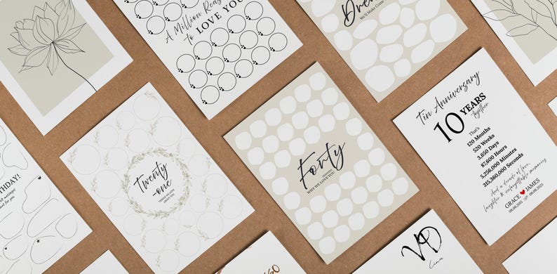 May include: A collection of white cards with various designs and text, including floral illustrations, the word "Forty," and anniversary details. The cards are arranged on a brown surface, creating a visually appealing display.