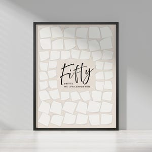 May include: A framed print with a beige background and a black border. The print features the word "Fifty" in elegant script, with the text "Things We Love About You" below. The background is filled with white, irregularly shaped squares.