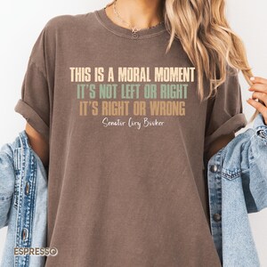 Op de afbeelding: Een bruin T-shirt met een citaat van senator Cory Booker: "Dit is een moreel moment. Het is niet links of rechts. Het is goed of fout."