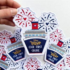 Op de afbeelding: Geborduurde patches met een cruiseschipontwerp en vuurwerk. De patches hebben een witte achtergrond met rode en blauwe accenten. De tekst "Disney WISH OUR FIRST CRUISE" staat op een marineblauwe banner.