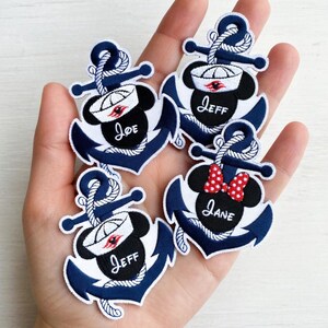 May include: Four navy blue anchor patches with white rope detailing. Each patch features a Mickey Mouse head wearing a sailor hat. The names "Joe", "Jeff", and "Jane" are embroidered on the patches.
