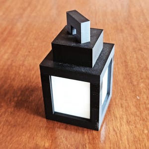 Pode incluir: Uma lanterna preta com uma alça no topo. A lanterna é feita de plástico e tem um interior branco.