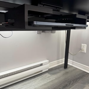 Könnte beinhalten: Ein schwarzes Computertablett unter dem Schreibtisch mit einem Laptop darin. Das Tablett ist unter einem schwarzen Schreibtisch montiert und hat ein minimalistisches Design. Der Laptop ist silberfarben und das Tablett ist aus Metall.