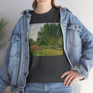 Peut inclure: Un t-shirt gris foncé avec une peinture vintage d'un paysage avec des arbres et des meules de foin. La peinture est dans un cadre rectangulaire et est centrée sur le t-shirt.