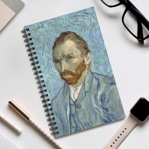May include: Spiral-bound notebook featuring a portrait of Vincent van Gogh. The artwork depicts the artist in a blue suit against a swirling blue background. The notebook is open, displaying the full image of the painting.