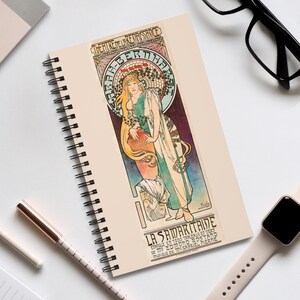 May include: A spiral-bound notebook with an Art Nouveau design. The illustration depicts a woman in flowing robes, with the text "THEATRE DE LA RENAISSANCE" and "LA SAMARITAINE". The artwork uses gold, green, and blue tones.