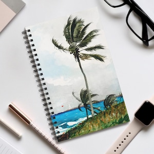 May include: Spiral-bound notebook with a watercolour painting of a tropical beach scene. The artwork shows palm trees, blue ocean waves, and a lighthouse under a cloudy sky. The notebook is open, displaying the artwork, with a pen and watch nearby.