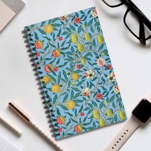 May include: A spiral-bound notebook with a light blue cover featuring a botanical pattern of oranges, lemons, and flowers. The design includes green leaves and red and white blossoms. The notebook is open, revealing the spiral binding.