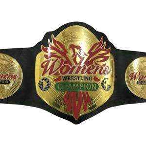 May include: A black championship belt featuring a large central gold plate with a red phoenix emblem and the text "Womens WRESTLING CHAMPION" in red and green. Two smaller circular gold plates on the sides also display "Womens CHAMPION".