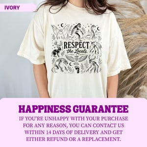 May include: An ivory short-sleeve t-shirt featuring a black graphic print of various mythical creatures including Bigfoot, a mothman, and a jackalope. The central text reads "RESPECT the Locals" surrounded by stars, moons, and forest elements.