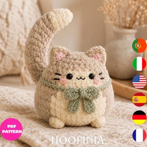 Peut inclure: Un jouet en peluche chat crocheté et rond avec un corps beige et crème, une longue queue courbée et un nœud vert sauge autour du cou. Le chat a des yeux brodés noirs, une petite bouche et des joues roses. Le texte PDF PATTERN HOOPINIA est visible.