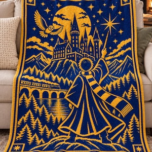 Pode incluir: Uma manta de crochê retangular em azul profundo e amarelo dourado com uma cena de uma figura de manto e cachecol listrado segurando uma varinha em direção a um castelo, uma lua cheia, uma coruja voando, um trem a vapor e uma floresta.