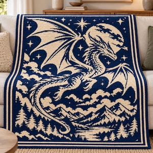 May include: A rectangular crochet blanket featuring a dark navy blue and cream color scheme. The design depicts a large dragon flying in front of a full moon, surrounded by stars, clouds, a mountain range, and a forest of pine trees below.