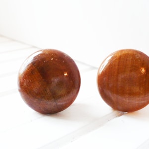 May include: Two round wooden knobs with a brown and orange wood grain pattern.
