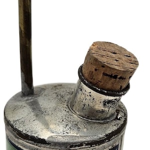 Könnte beinhalten: Vintage Radius Automatikkanister mit gebogenem Messingauslauf und Korken. Die Dose ist silber-grün mit dem Wort "RADIUS" in einem goldenen Etikett. Der Text auf der Dose lautet "AUTOMATIC CAN".