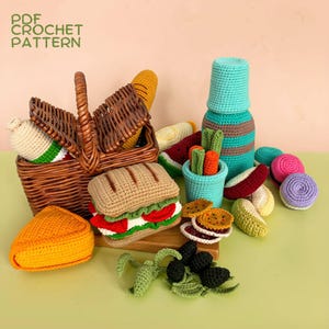 Op de afbeelding: Een verzameling gehaakte speelgoedvoedingsmiddelen, waaronder een sandwich, een stuk kaas, olijven, macarons en een fles, gerangschikt bij een bruine rieten picknickmand. De tekst PDF CROCHET PATTERN is zichtbaar in de linkerbovenhoek.