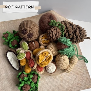 May include: A collection of crocheted items representing various nuts and seeds, including a pinecone, walnuts, peanuts, and acorns with green leaves. A white label in the top left corner features the black text PDF PATTERN.