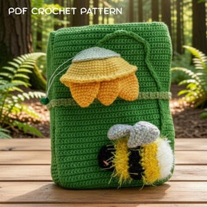May include: A green crochet cover featuring the text PDF CROCHET PATTERN at the top. The cover is decorated with a three-dimensional yellow flower and a fuzzy bumblebee with black, yellow, and white stripes and grey wings attached to the front.
