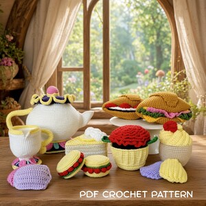 May include: A collection of crocheted play food items including a white teapot, a creamer, a slice of cake, a cupcake, a sandwich, a croissant, and small cookies. The items are crafted with yarn in various colors. Text reads: PDF CROCHET PATTERN.