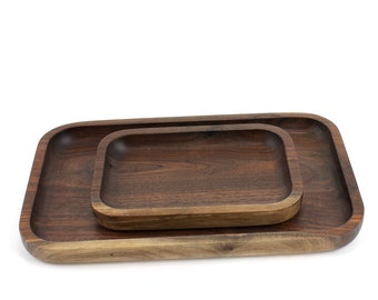 May include: Two rectangular wooden serving trays, one nested inside the other. The trays are made of dark brown walnut wood and have a smooth, polished finish.