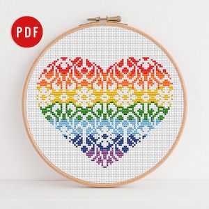 May include: A rainbow heart cross stitch pattern in a wooden embroidery hoop. The heart is made up of a rainbow of colors, with each color having a different pattern.