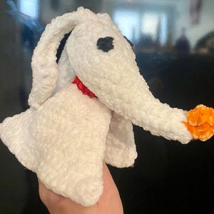 May include: A handmade plush toy of Zero, the ghost dog from The Nightmare Before Christmas. The plush is primarily white with a long, curved nose, black eyes, and an orange nose. It has a red collar.