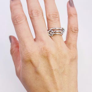 以下が含まれることがあります： シルバーリング、ユニークなデザインで相互接続されたループが特徴です。指に装着され、その複雑なディテールと洗練された仕上がりを際立たせています。リングのデザインはモダンで人目を引きます。