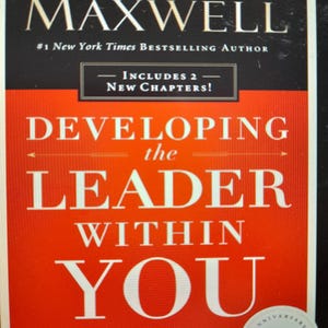 May include: Book cover with a red background and white text that reads "Developing the Leader Within You". The book is by John C. Maxwell and is a #1 New York Times Bestselling Author. The cover also includes the text "Includes 2 New Chapters!" and "Revised and Updated, Over 2 Million Copies Sold". The cover also features a 25th Anniversary Edition seal.
