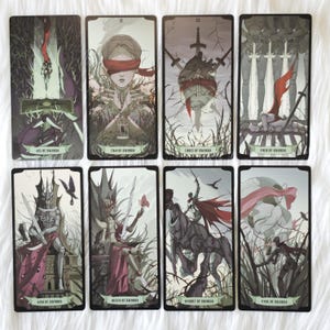 May include: A set of eight tarot cards from the suit of swords, featuring dark, illustrative artwork with muted tones of gray, green, and red. Each card displays a unique scene with swords, figures, and thorny branches, labeled with titles like Ace of Swords.