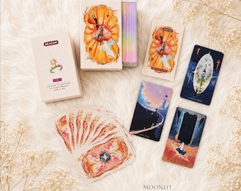 May include: A deck of Beacon tarot cards featuring a box with a lighthouse illustration, an instruction booklet, and several cards displaying celestial and nautical imagery. The card edges are iridescent, and the set includes cards titled The Magician, The Fool, and The High Priestess.