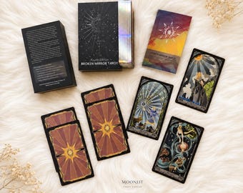 May include: A Broken Mirror Tarot deck, fourth edition, featuring a black box with silver edges, a colorful guidebook, and several tarot cards with intricate illustrations. The cards display various scenes, including figures and celestial motifs.