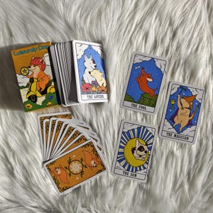 May include: A deck of tarot cards featuring dog illustrations. The cards include images of dogs on a scooter, and cards labeled "The Lovers", "The Fool", "The Magician", and "The Sun". The card backs have a repeating dog and star design.