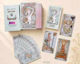 May include: A Moravia tarot deck set featuring a light green box with ornate floral borders, a matching instruction booklet, and several rectangular cards displaying detailed illustrations of figures in flowing robes with celestial and botanical motifs.