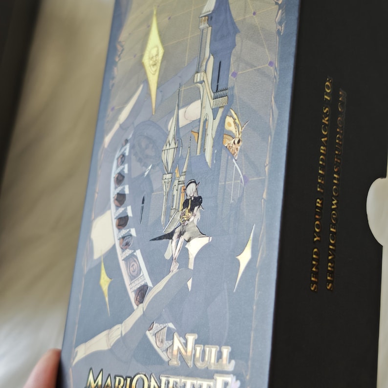 May include: A rectangular box with a dark blue and black cover featuring a detailed illustration of a character, architectural structures, and star shapes. The text "NULL MARIONETTE" is printed at the bottom, and "SEND YOUR FEEDBACKS TO: SERVICE@WOHSTUDIO.CN" is printed in gold on the side.