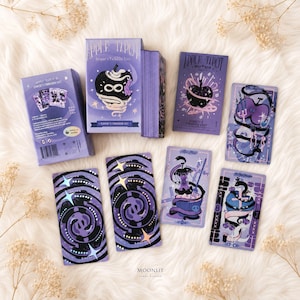 Puede incluir: Una baraja de cartas de tarot Apple titulada Serpent's Forbidden Lost, con ilustraciones en morado y negro de manzanas, serpientes y motivos celestiales. El set incluye una caja rectangular, un mazo de cartas y varias cartas de tarot sueltas.