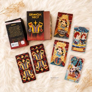 May include: A Dramagiac Tarot deck featuring a black box with a jester hat graphic, gold-edged cards, and individual tarot cards displaying colourful illustrations of animals in circus-themed settings, including The Fool and The Lovers cards.