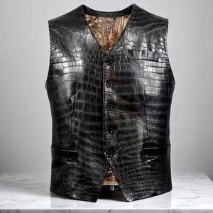 May include: A black leather vest with a crocodile skin texture. The vest has a V-neck, four buttons, and two front pockets. The interior lining is a patterned tan fabric. The vest is displayed on a white surface.