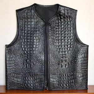 May include: Black leather vest with a crocodile skin texture. The vest features a V-neck and a full-length zip. The sleeveless vest appears to be made of genuine leather.