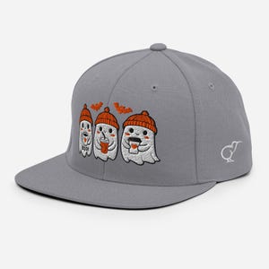 Könnte beinhalten: Eine graue Baseballkappe mit einer Stickerei von drei weißen Geistern, die orangefarbene Mützen tragen und Kaffeetassen halten. Zwei kleine orangefarbene Fledermäuse sind darüber gestickt und ein weißes Kiwi-Vogel-Logo befindet sich an der Seite.